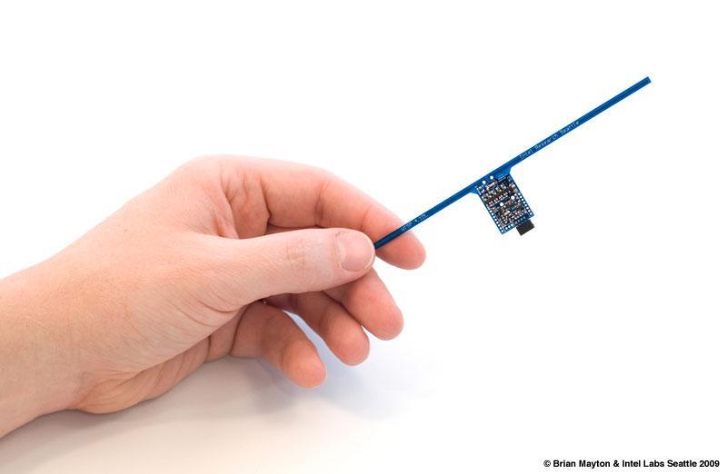 a hand holding a blue circuit board with long antennas