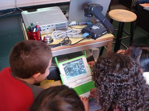 three students gathered around an XO laptop