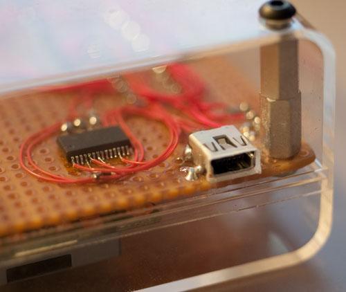 photo through the clear plastic case showing the USB jack and the FTDI
    chip, with little wires soldered to the pins